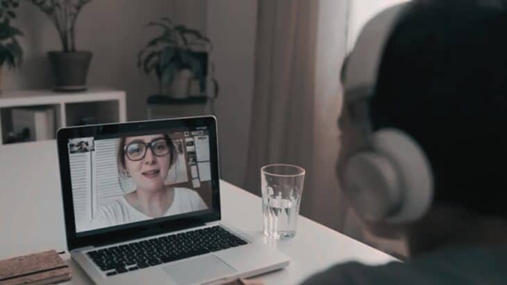 A Man Participates in A Webinar, Watching a Presenter on His Laptop Screen While Wearing Headphones in A Home Office Setting