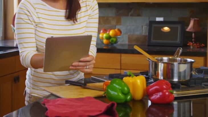 A Nutritionist Using a Tablet in A Kitchen with Colorful Bell Peppers on The Counter