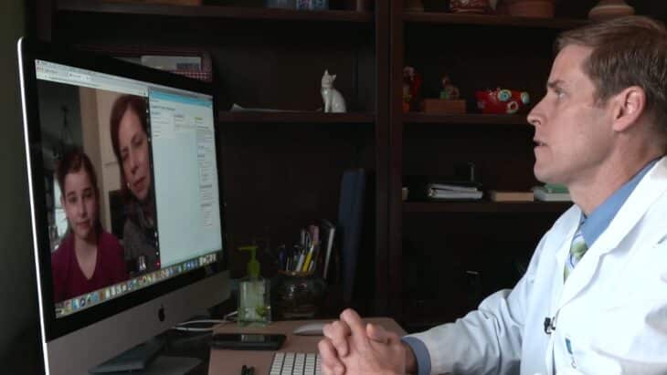 A Doctor Conducts a Telehealth Consultation with A Mother and Daughter via Computer in His Office