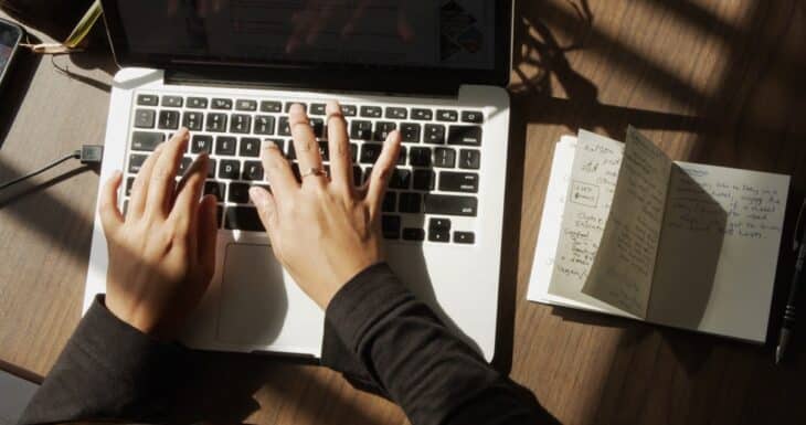 Typing on a laptop while an authentic handwritten note is placed beside it