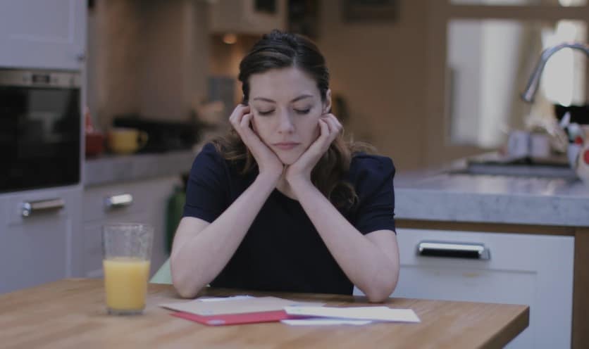 A woman, head in hands, lost in paperwork, a quiet kitchen scene