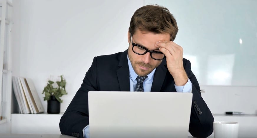 A man in a suit, head in hand, deeply engrossed in work