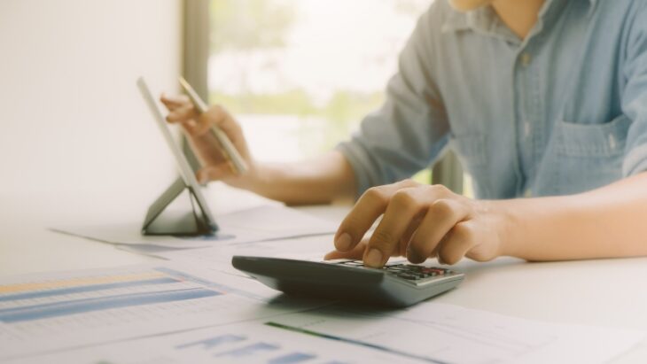 Person using a calculator and reviewing documents to set up better invoicing practices and prevent future issues with clients ignoring invoices