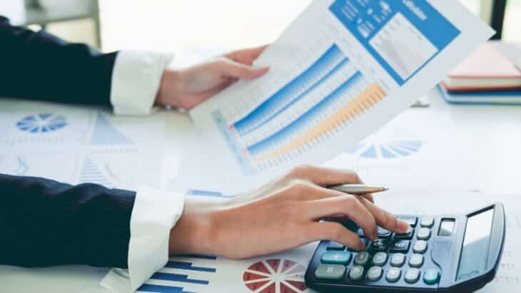 Person reviewing financial charts and using a calculator to reassess their invoice process