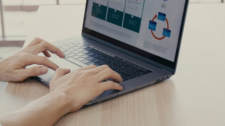 Hands typing on a laptop with a clear infographic displayed on the screen, emphasizing structure and clarity