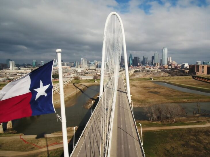 Iconic bridge and Texas flag with Dallas skyline in the background, rent prices still competitive in parts of the city