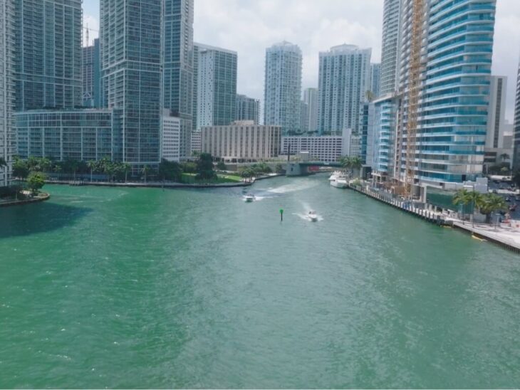 Boats navigating the Miami River surrounded by skyscrapers, highlighting rising rent prices in coastal zones