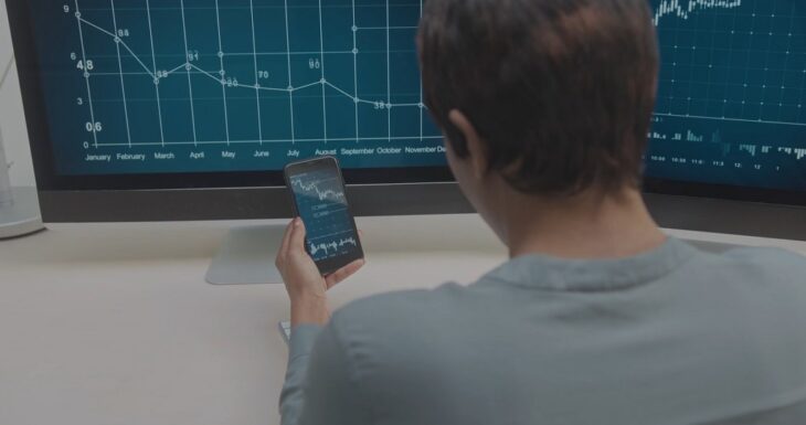 A person analyzing compliance audit data on a mobile phone and computer screen
