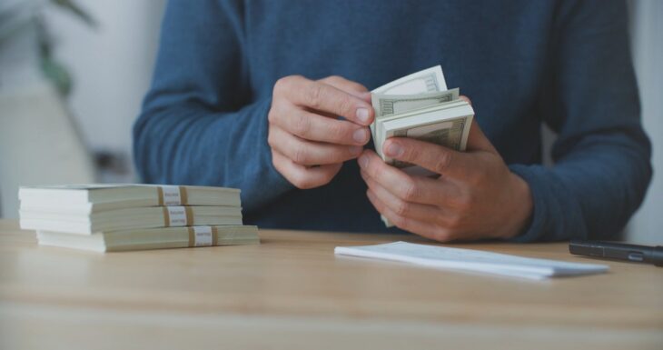 Person counting stacks of US dollar bills on a wooden table
