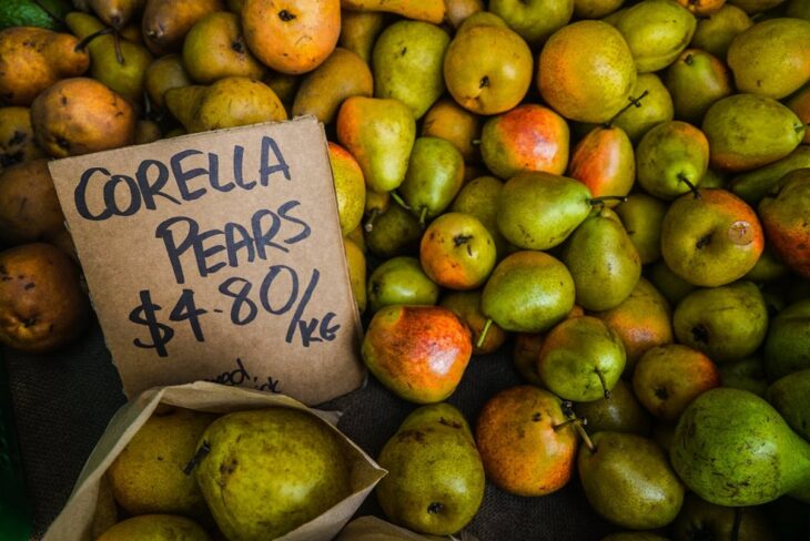 Fresh Corella pears displayed with a handwritten price sign at a market
