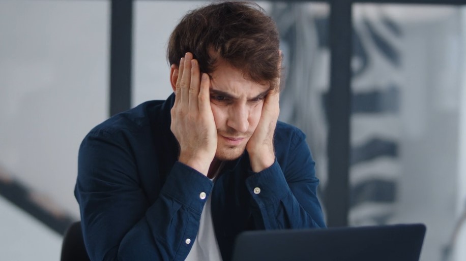 A man sitting at a desk, visibly distressed, with his head in his hands, suggesting feelings of overwhelm or frustration
