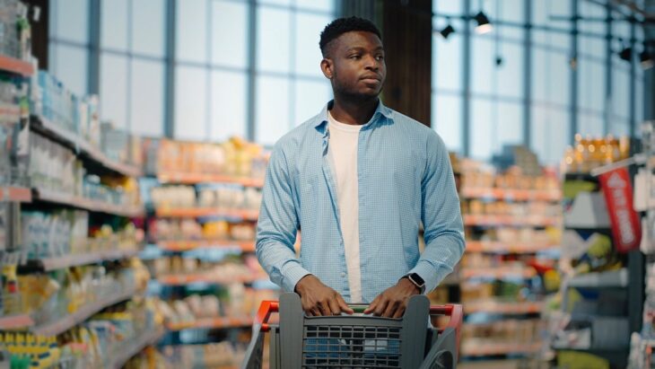 Young man with a shopping cart in a supermarket, reflecting the idea of where to buy time