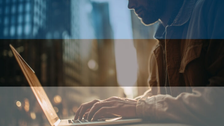 Freelancer in Tallinn using a laptop, medieval towers and modern glass buildings blurred in the background