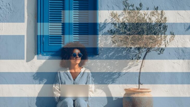 Female freelancer with a laptop in front of whitewashed walls and blue shutters typical of Greece