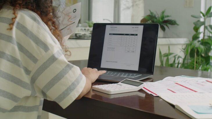 A person uses a laptop and calculator while reviewing bills and financial documents, highlighting the role of specialized software in financial management