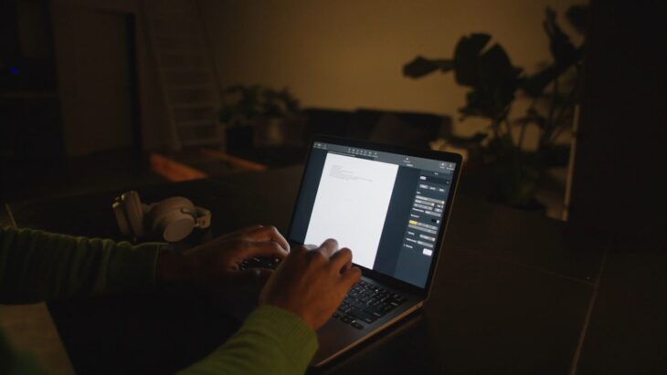 Person typing on a laptop in a dimly lit workspace, focusing on code and interface adjustments during late-night web design