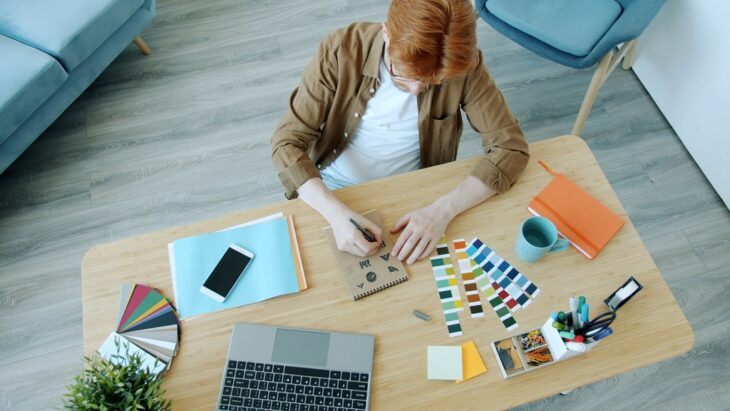 Creative designer choosing color palettes and sketching logo concepts at a bright home office desk, planning a new web design project