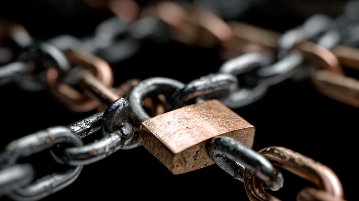 Close-up of metal chains secured with a brass padlock against a dark background