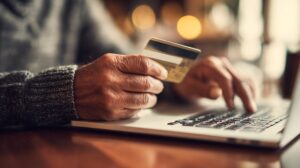 Close-up of a person holding a credit card while typing on a laptop keyboard