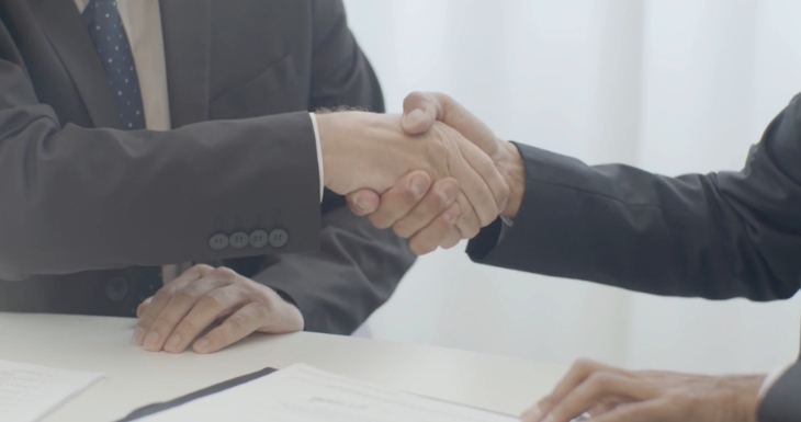 Two professionals shake hands over signed client documents