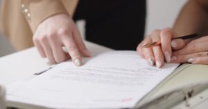 Hands review and sign paperwork on a desk for legal protection