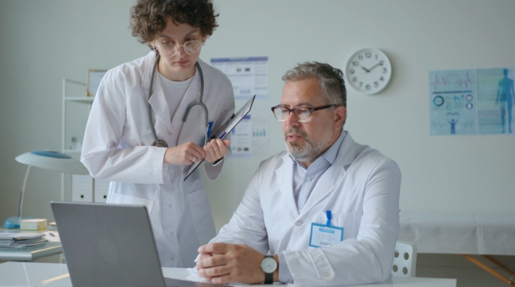 Doctors reviewing performance data on a laptop as part of healthcare business strategy planning in a clinical office