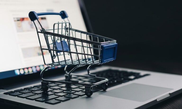 A miniature shopping cart sits on a laptop keyboard, symbolizing online shopping