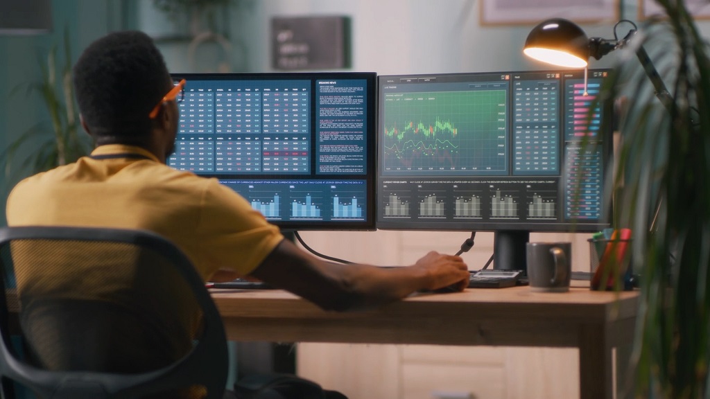 Trader analyzing financial market data and charts on a multi monitor trading platform setup