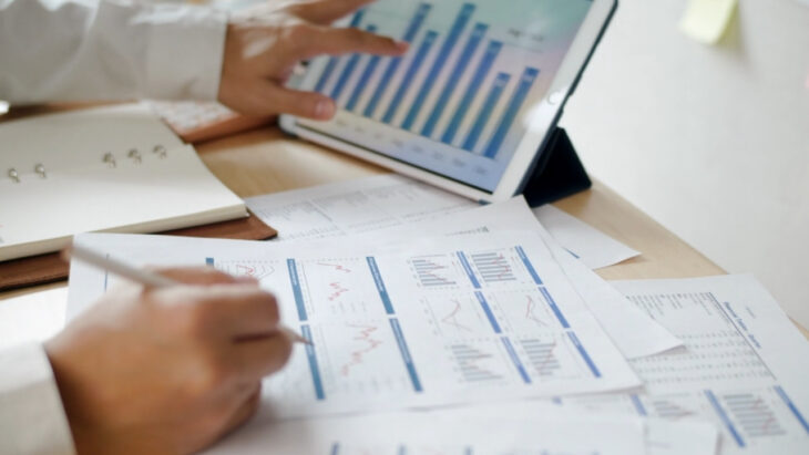 Investor reviewing financial charts and market data on a tablet and printed reports