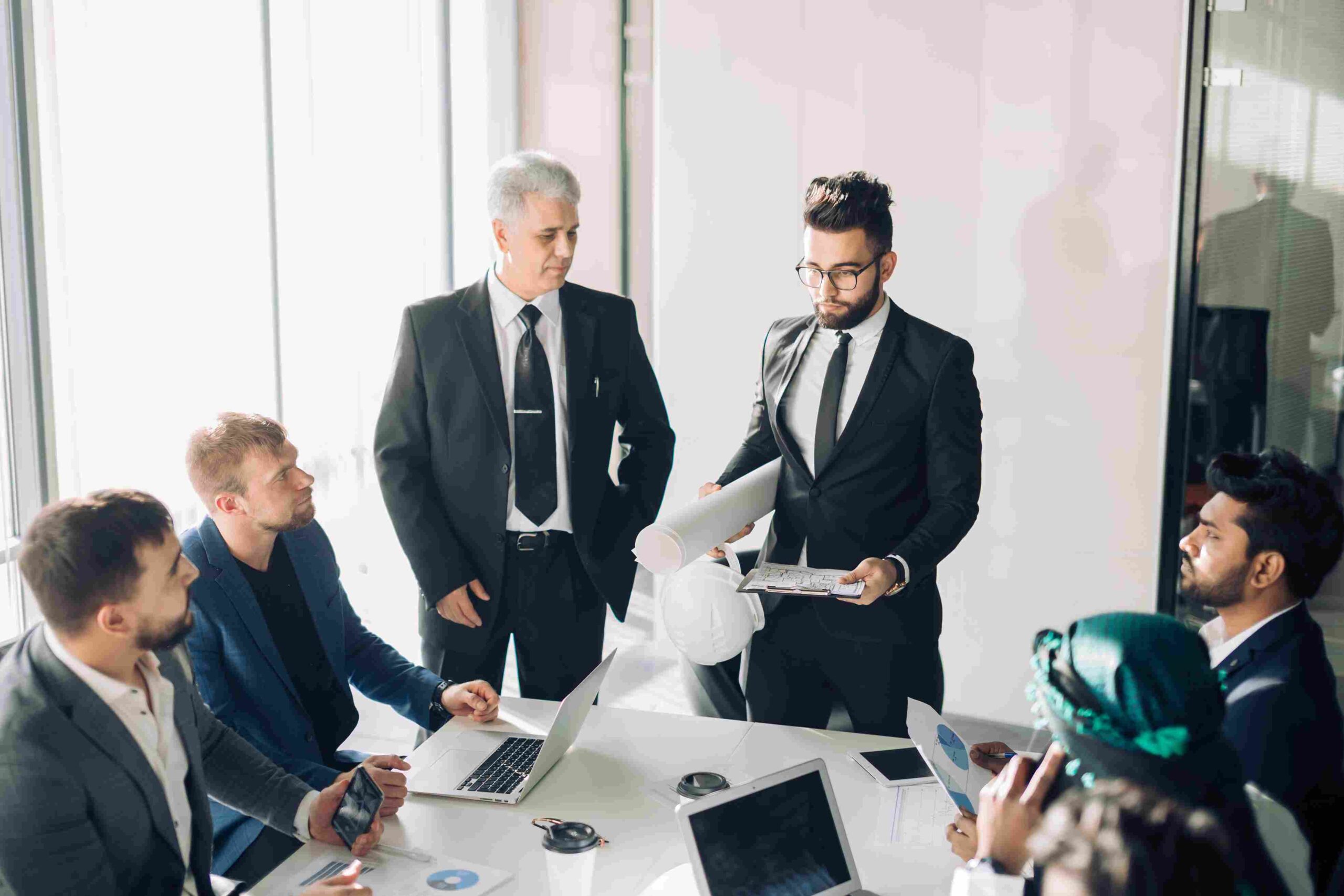 Six business professionals discussing documents and project plans around a conference table.