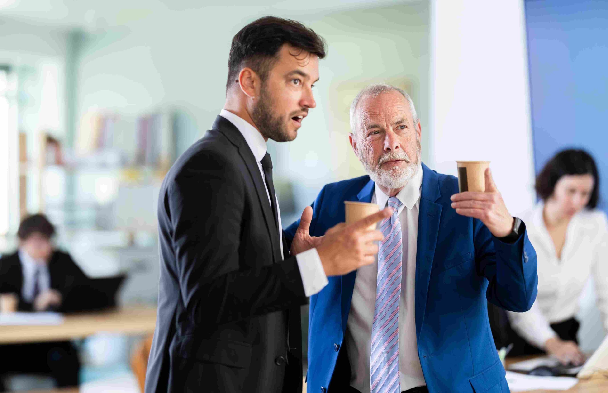 Two male business professionals in suits discussing work in a modern office.